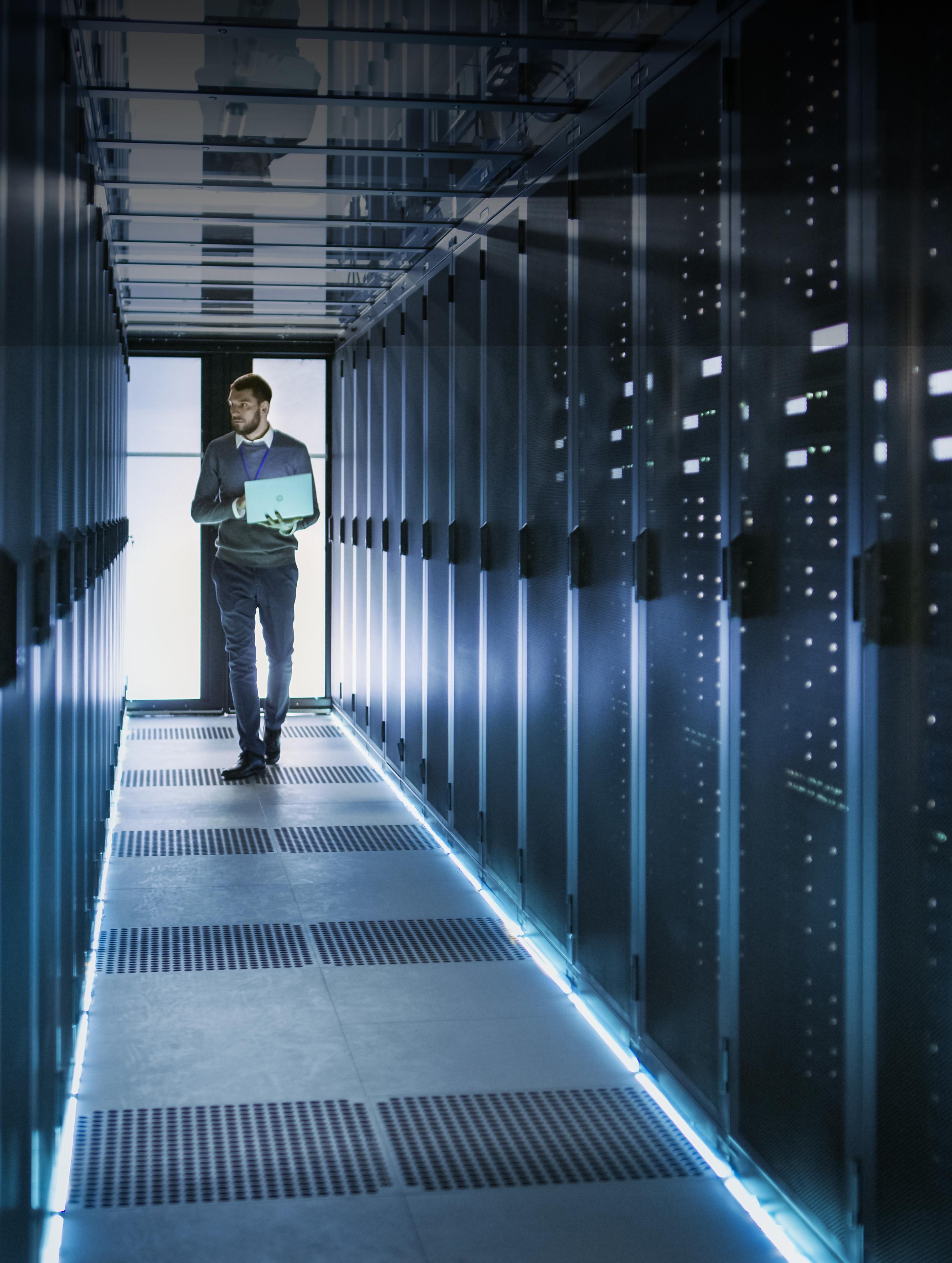 Das Bid zeigt einen Mann mit einem Laptop in der Hand, der einen Flur mit ganz vielen Superrechner entlang läuft.