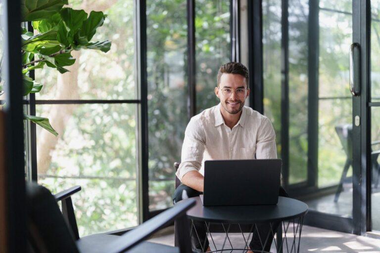 Das Bildmotiv zeigt einen lachenden Mann im Büro vor seinem Laptop